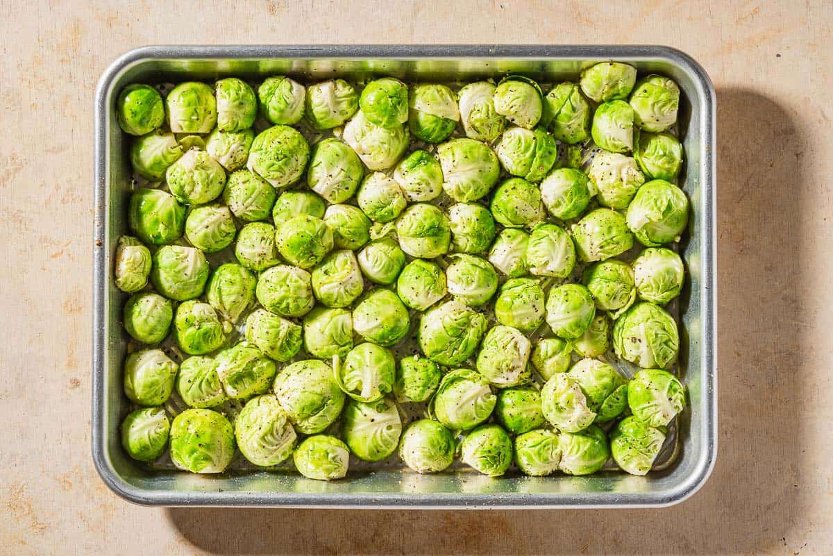 An overhead photo of uncooked brussels sprouts seasons with salt and pepper spread in one layer on a baking sheet.