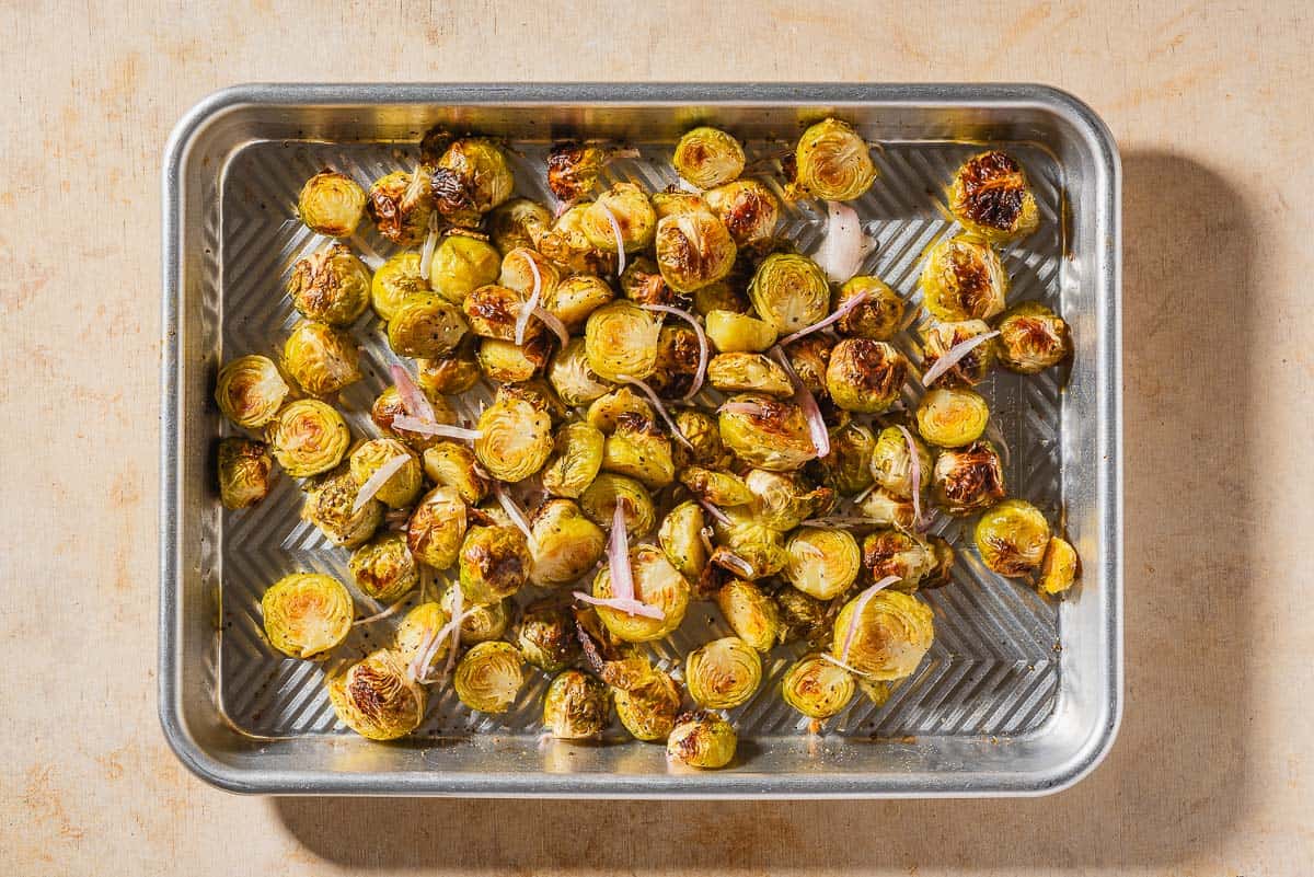 On overhead photo of roasted brussels sprouts with shallots spread evenly on a baking sheet.