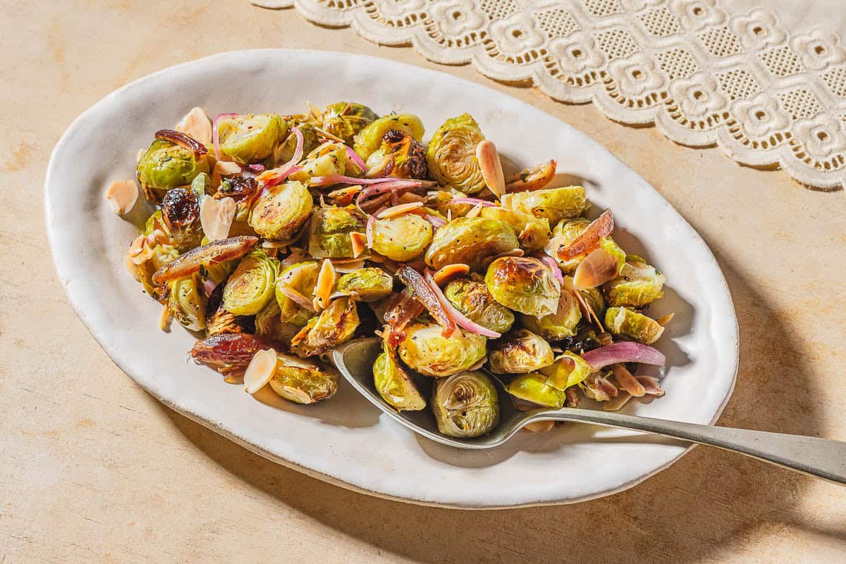 Roasted brussels sprouts with dates and almonds on a platter with a spoon.