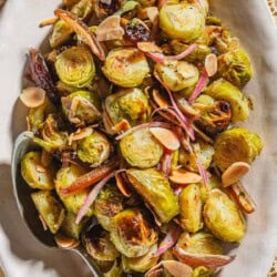 An overhead photo of roasted brussels sprouts with dates and almonds on a platter with a spoon.