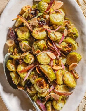 An overhead photo of roasted brussels sprouts with dates and almonds on a platter with a spoon.