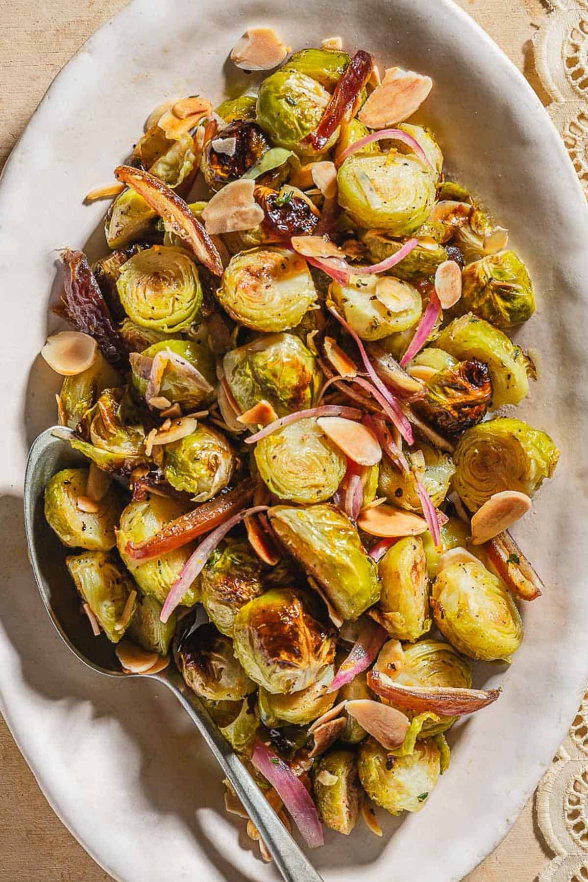 An overhead photo of roasted brussels sprouts with dates and almonds on a platter with a spoon.