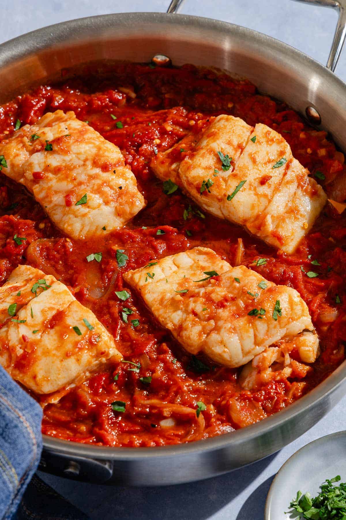 A close up of tomato sauce poached cod fillets in a skillet.