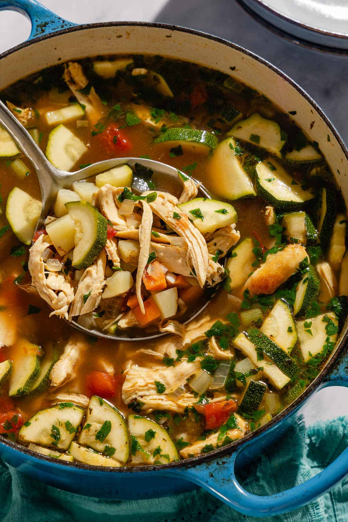 A close up of chicken vegetables soup in a dutch oven with a ladel.