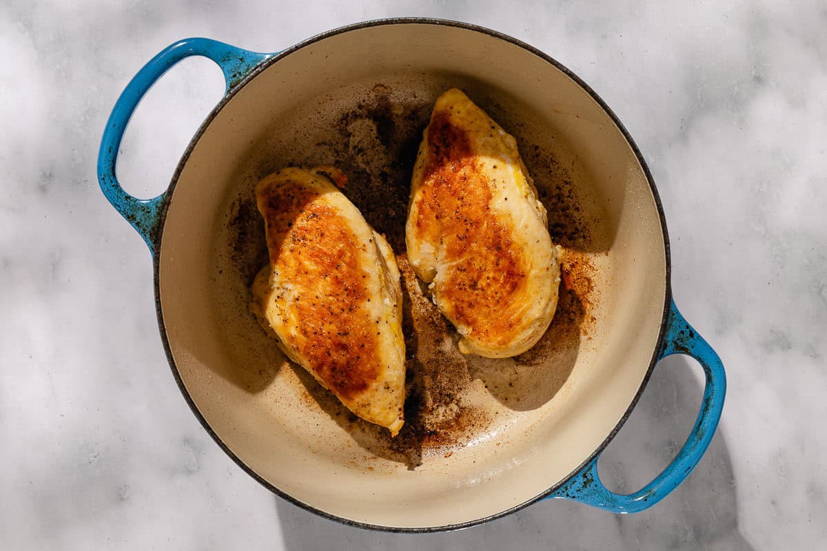 An overhead photo of 2 chicken breasts being cooked in a dutch oven.