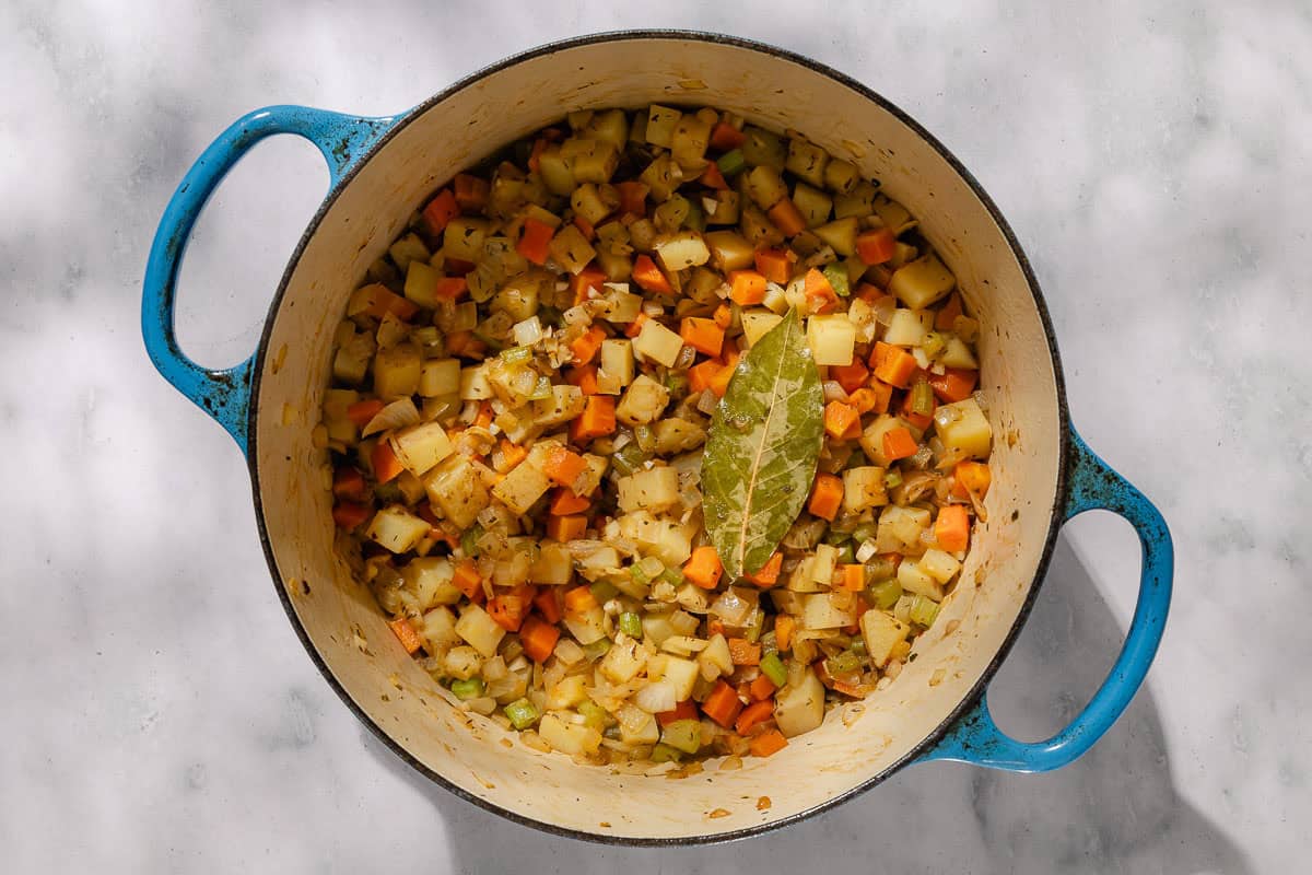 An overhead photo of sauteed chopped vegetables and a bay leaf in a dutch oven.