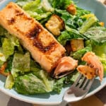 A close up of salmon caesar salad in a bowl with a fork.