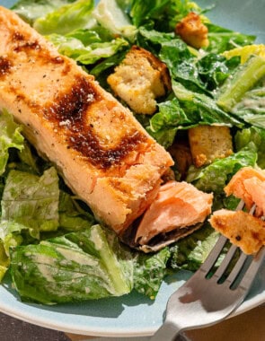 A close up of salmon caesar salad in a bowl with a fork.