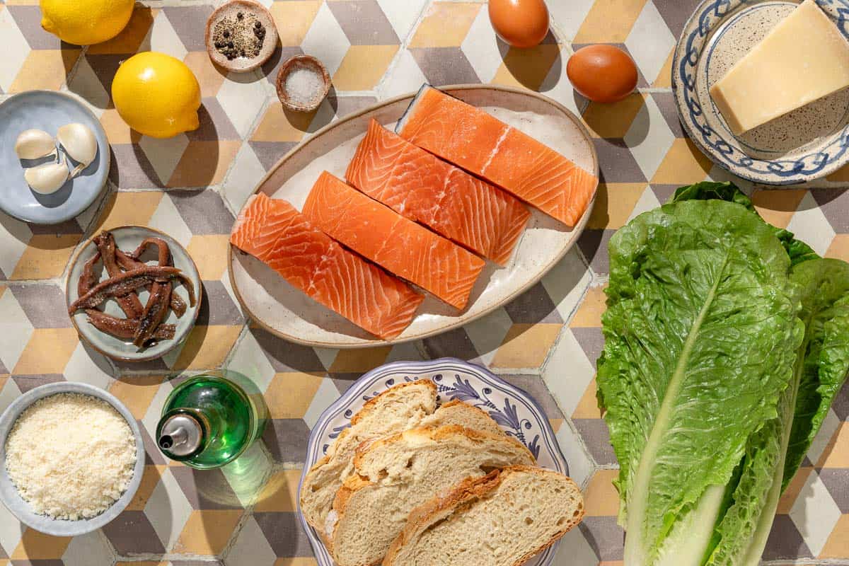 Ingredients for salmon caesar salad including 4 salmon filets, salt, black pepper, anchovy filets, garlic, eggs, parmesan cheese, lemons, olive oil, bread, and romaine lettuce.