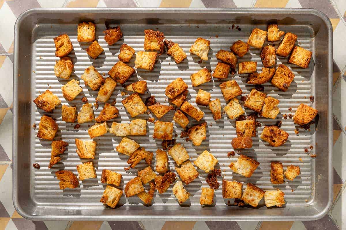 An overhead photo of baked croutons spread evenly on a sheet pan.