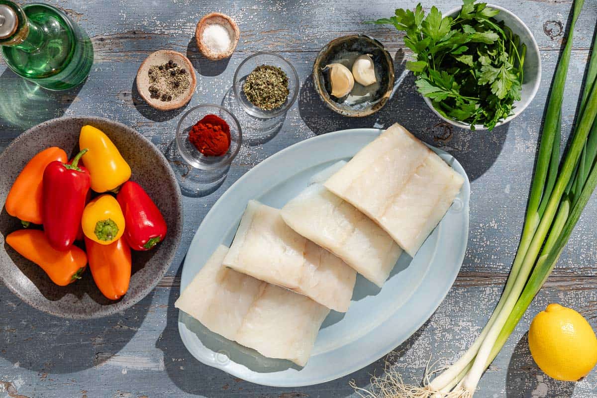 Ingredients for baked haddock with baby bell peppers including 4 halibut fillets, salt, black pepper, baby bell peppers, green onions, garlic, oregano, paprika, lemon, olive oil, and parsley.