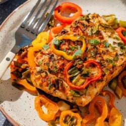 A close up of a serving of baked haddock with baby bell peppers on a plate with a fork.