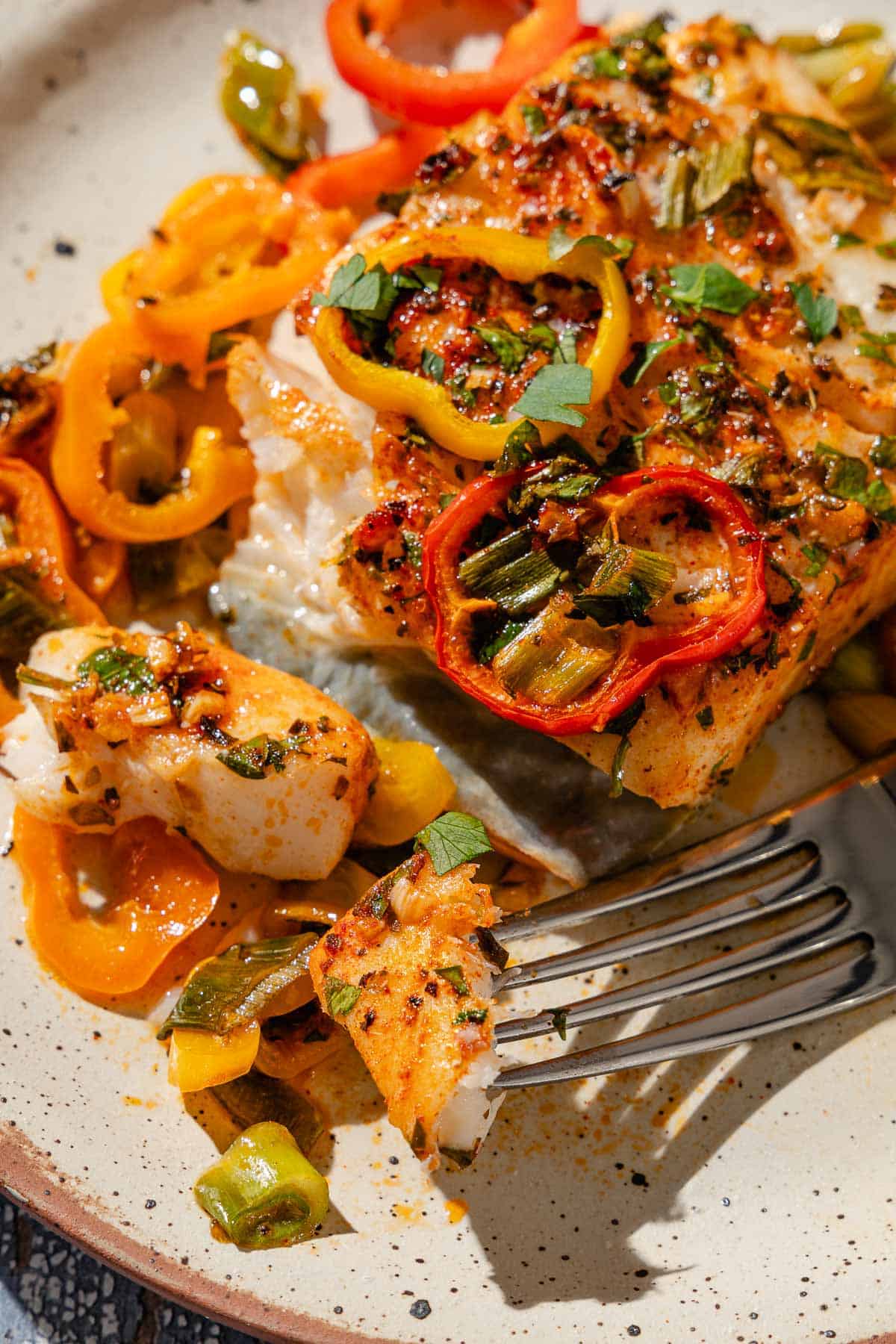 A close up of a serving of baked haddock with baby bell peppers on a plate with a fork.