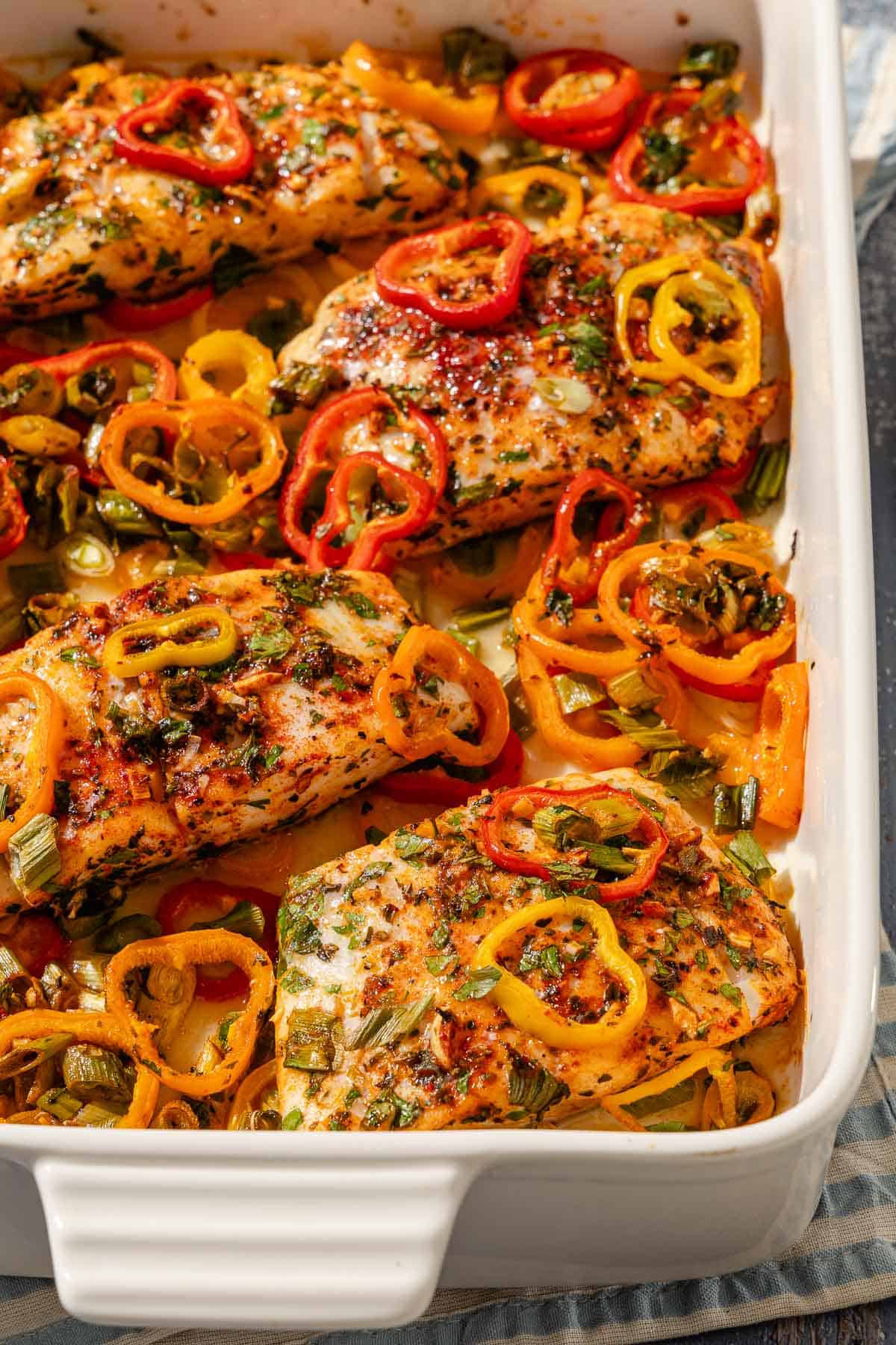 A close up of baked haddock with baby bell peppers in a baking dish.