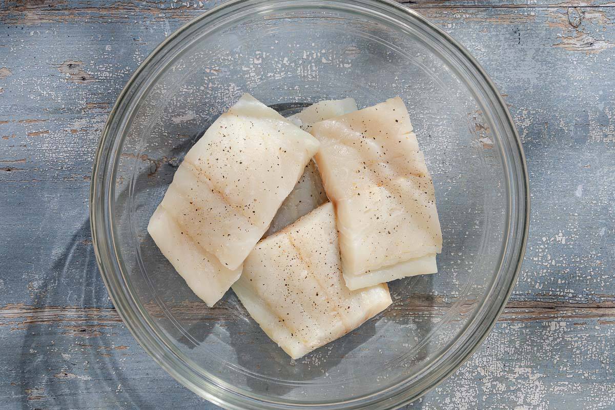 An overhead photo of the haddock fillets seasoned with salt and black pepper in a bowl.