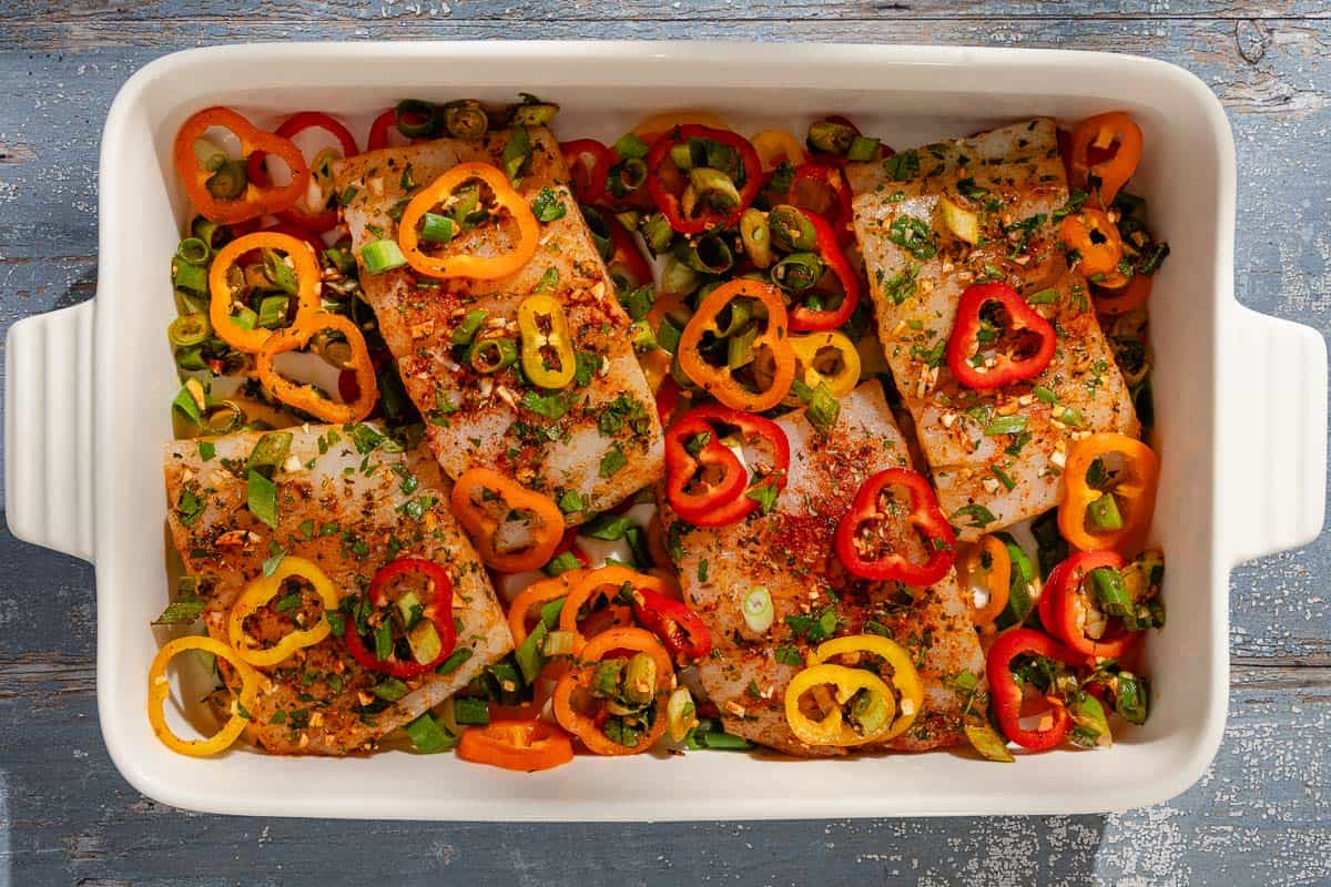 An overhead photo of uncooked haddock with baby bell peppers in a baking dish.