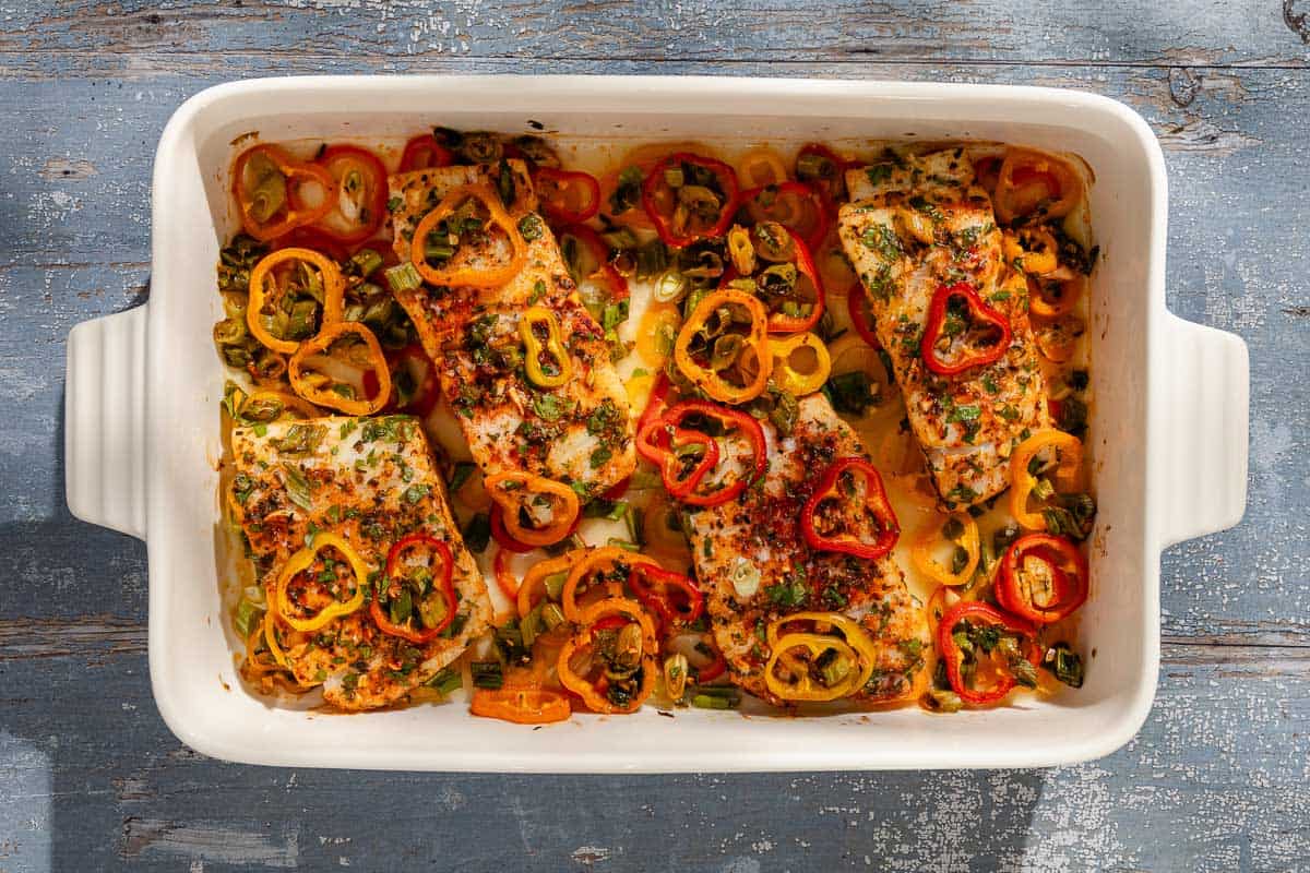 An overhead photo of baked haddock with baby bell peppers in a baking dish.