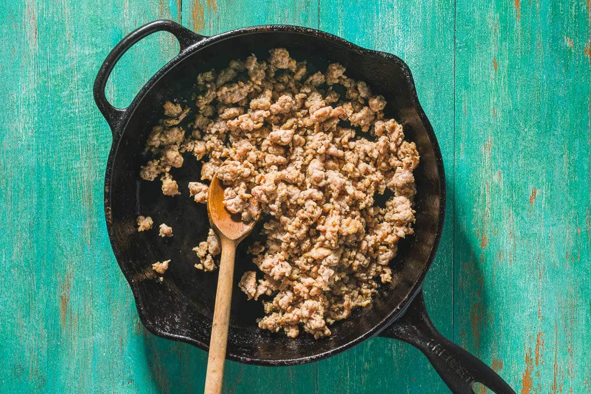 An overhead photo of the crumbled Italian turkey sausage being cooked in a skillet with a wooden spoon.