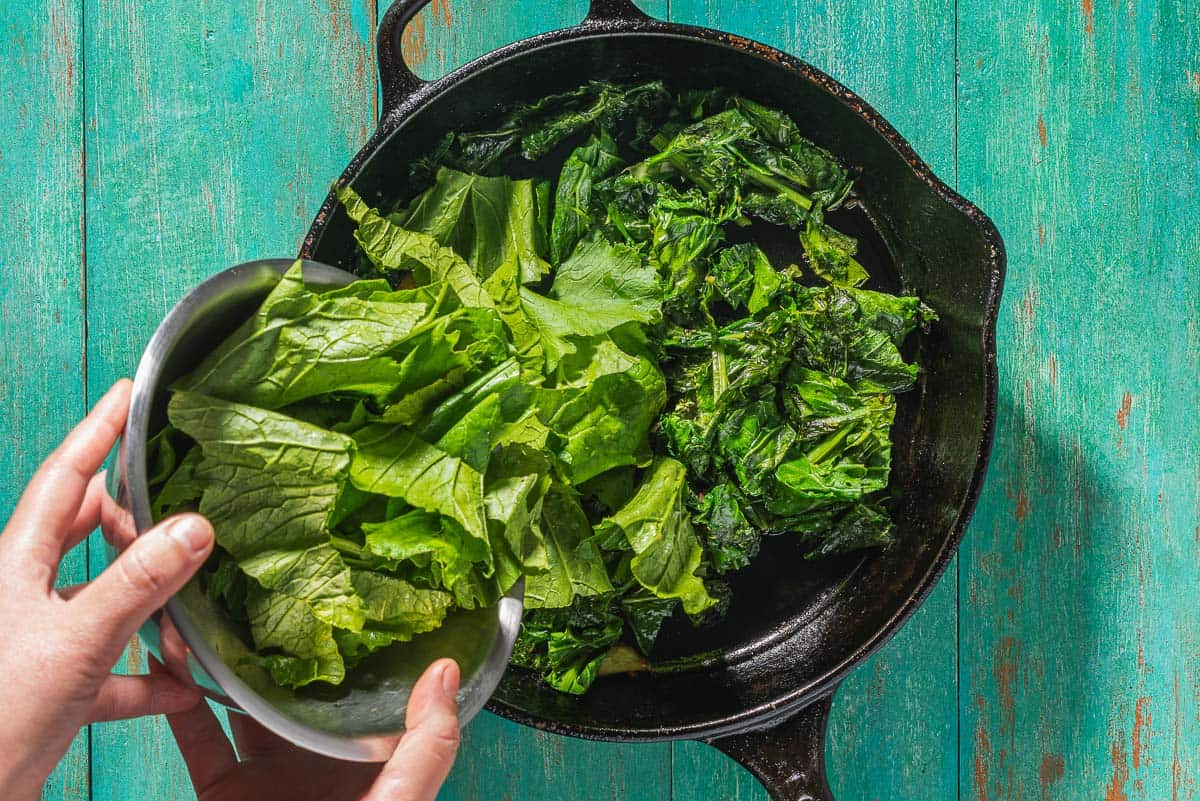 An overhead photo of the chopped broccoli rabe being poured from a bowl into a skillet.