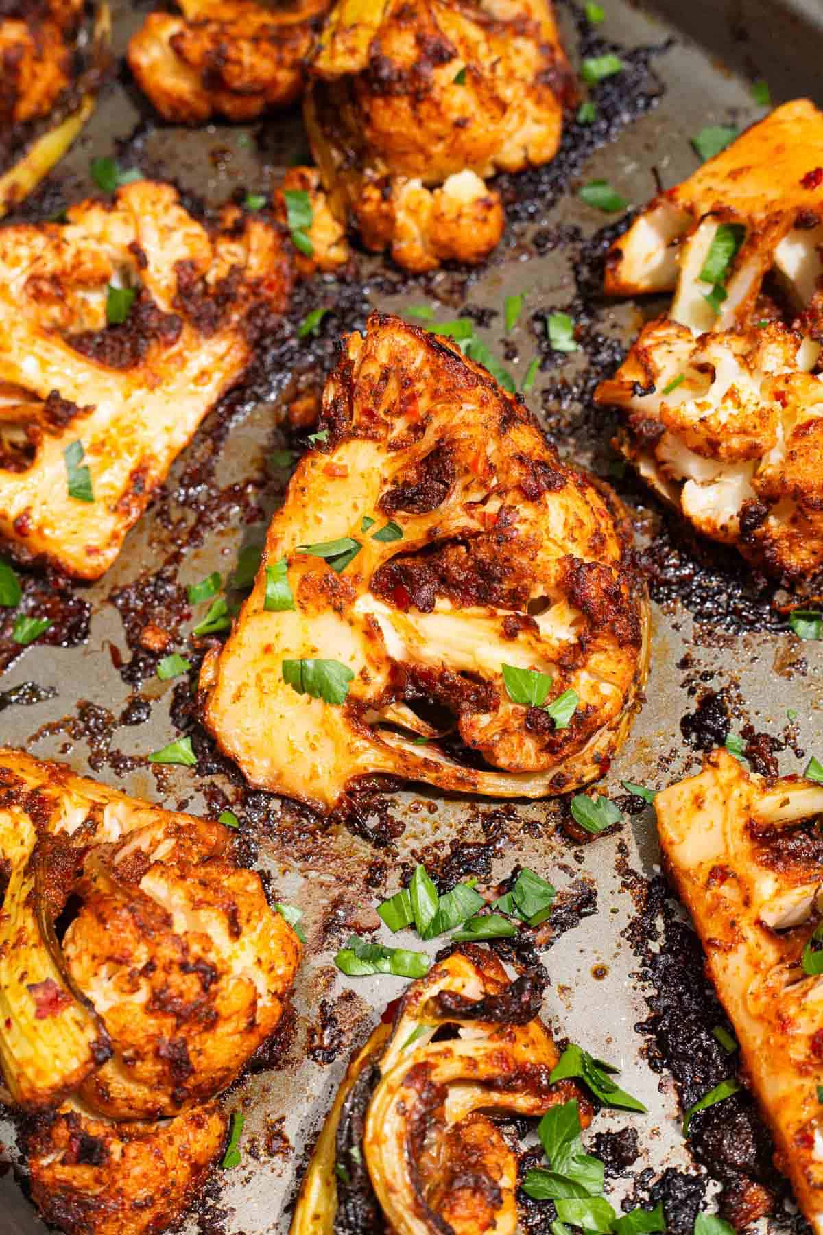 A close up of spicy baked cauliflower wedges topped with chopped parsley on a baking sheet.