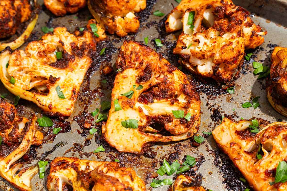 A close up of spicy baked cauliflower wedges topped with chopped parsley on a baking sheet.