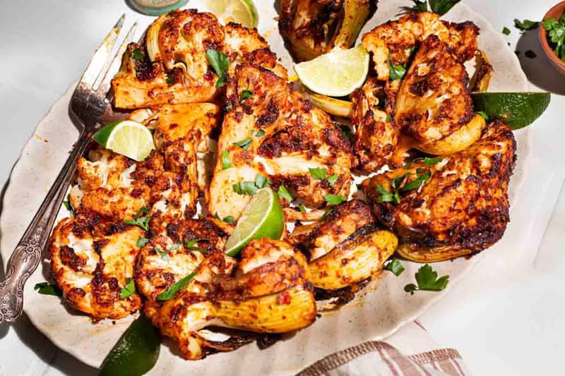 An overhead photo of spicy baked cauliflower topped with chopped parsley and lime wedges on a serving platter with a fork.