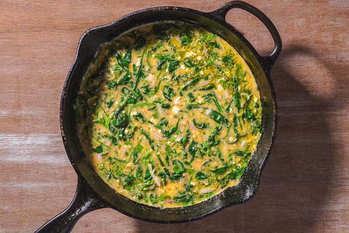 An overhead photo of and uncooked feta spinach frittata in a cast iron skillet.