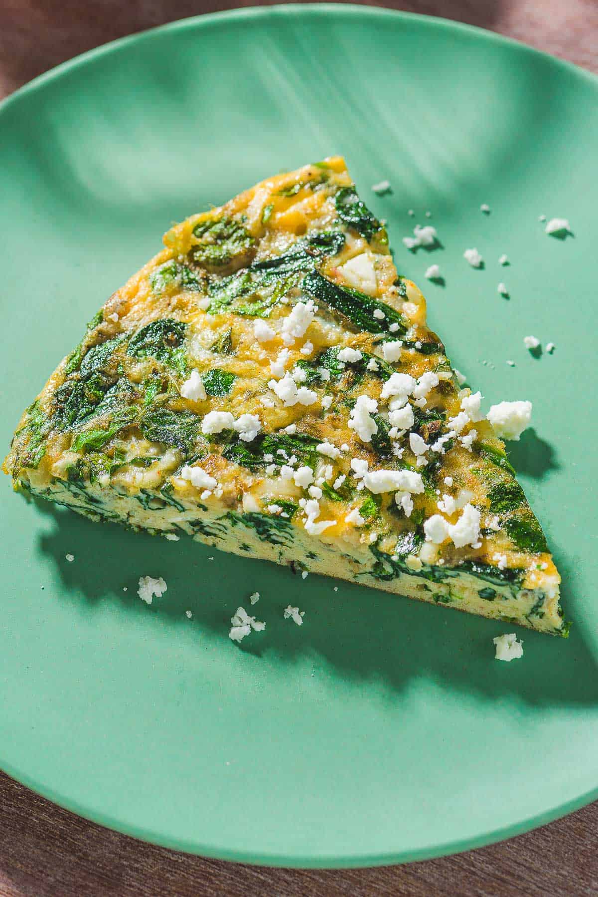 A close up of a slice of the feta spinach frittata topped with crumbled feta on a plate.