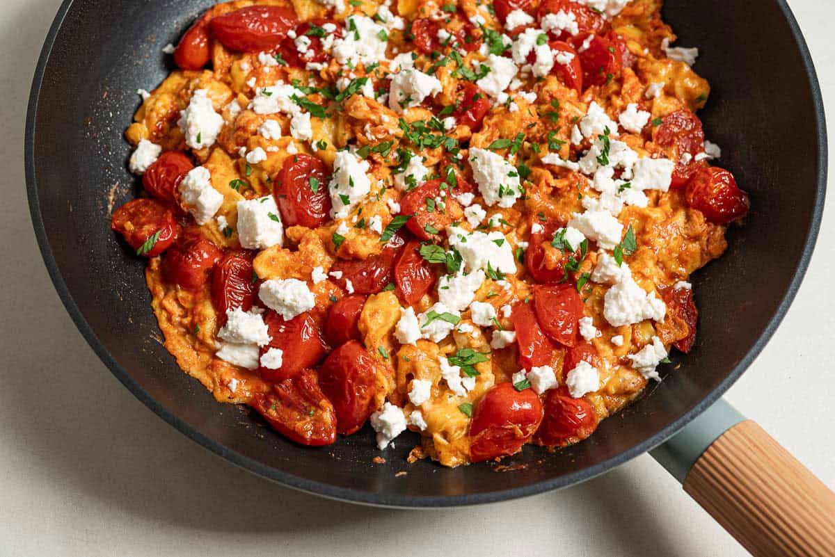 A close up of strapastada greek tomato scrambled eggs topped with crumbled feta and chopped parsley in a skillet.