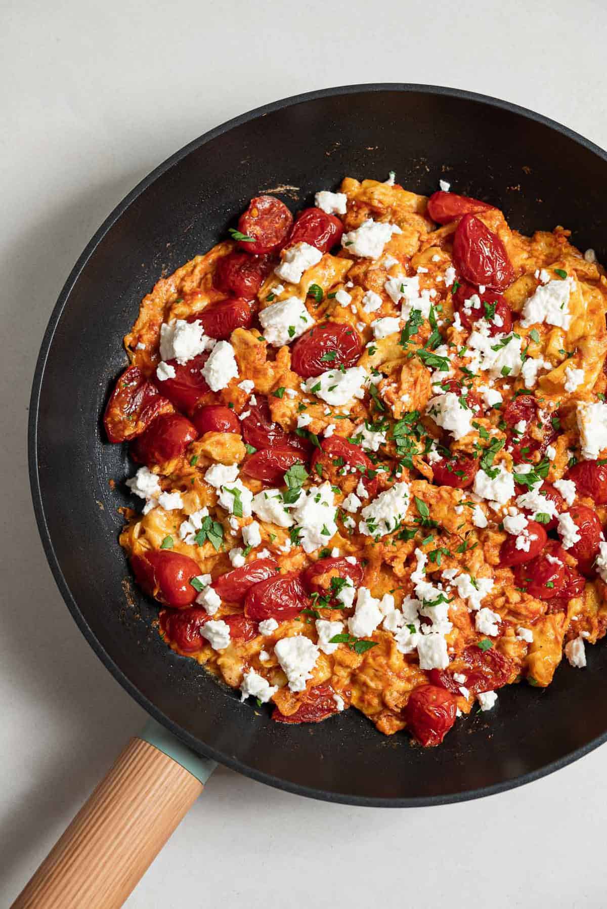 An overhead photo of strapastada greek tomato scrambled eggs topped with crumbled feta and chopped parsley in a skillet.