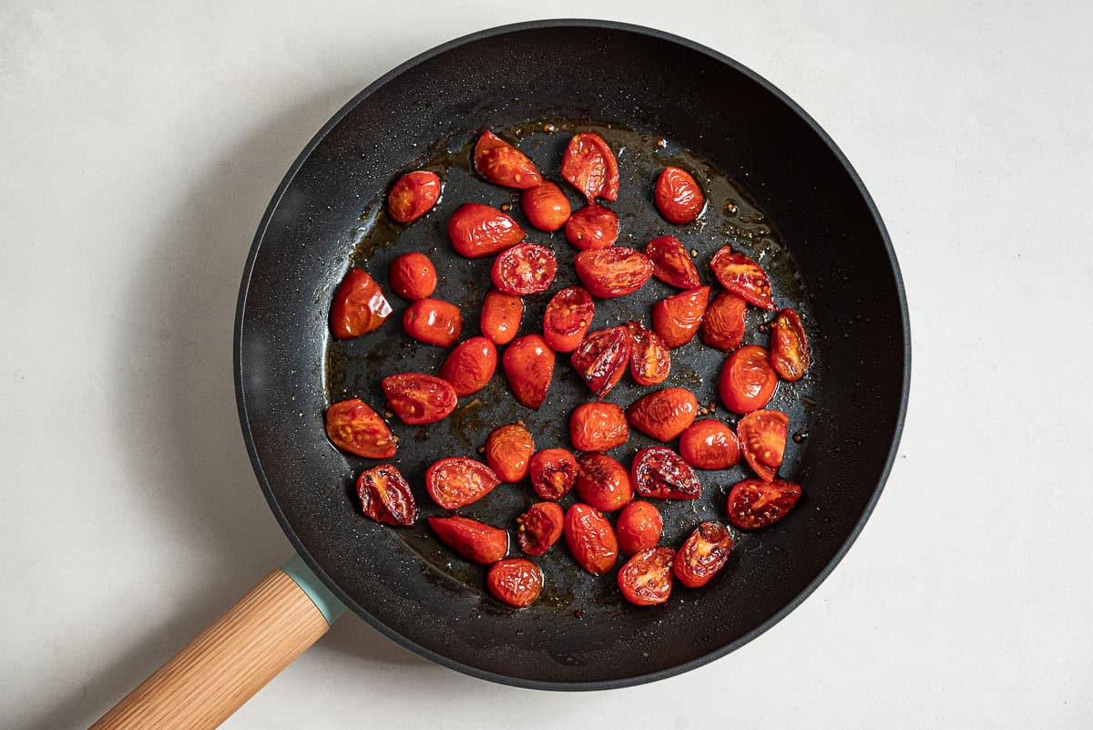 An overhead photo of halved cherry tomatoes being sauteed in a skillet.