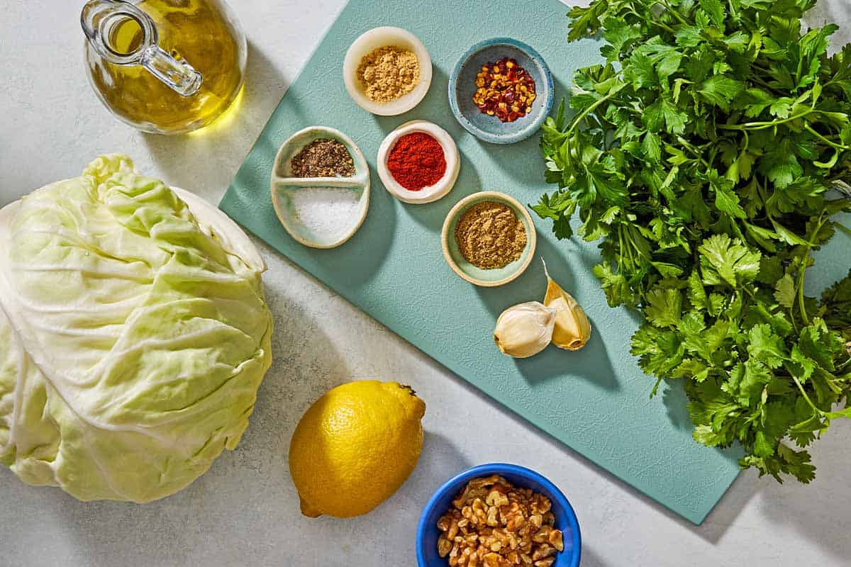 Ingredients for cabbage steaks with green chermoula and toasted walnuts including cabbage, walnuts, lemon, garlic, parsley, olive oil, salt, black pepper, cilantro, coriander, red pepper flakes, and ground ginger.