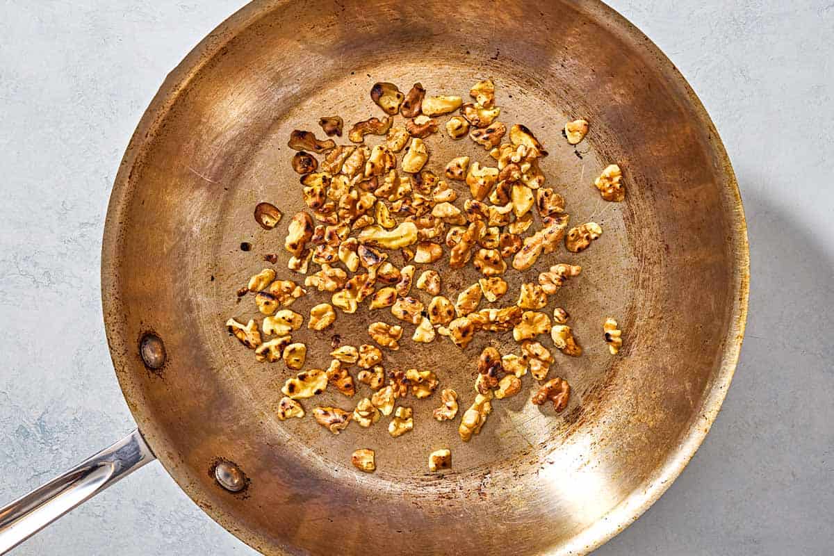 An overhead photo of walnuts being toasted in a skillet.