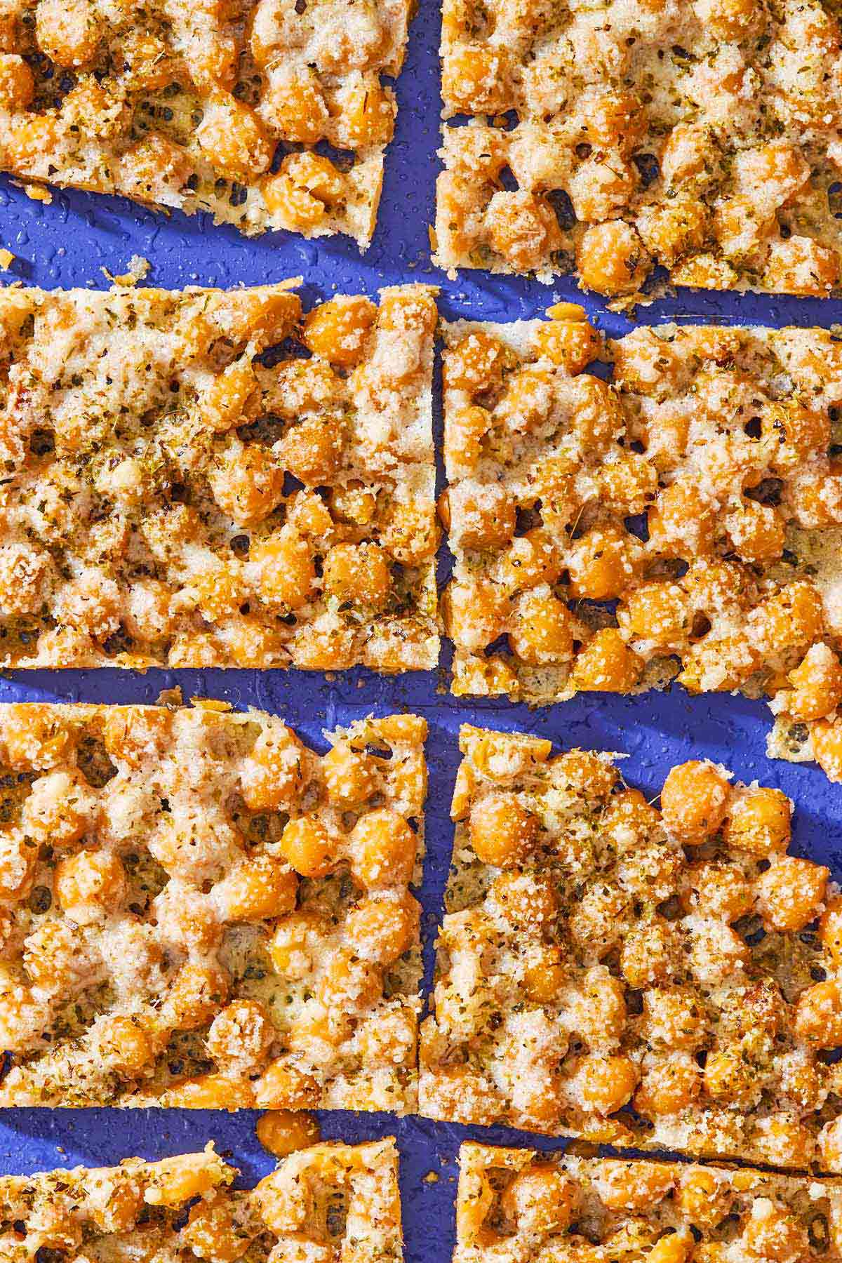 An overhead photo of baked parmesan crisps with chickpeas and oregano cut into 8 slices.