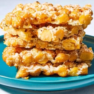 A close up of a stack of 5 baked parmesan crisps with chickpeas and oregano on a plate.