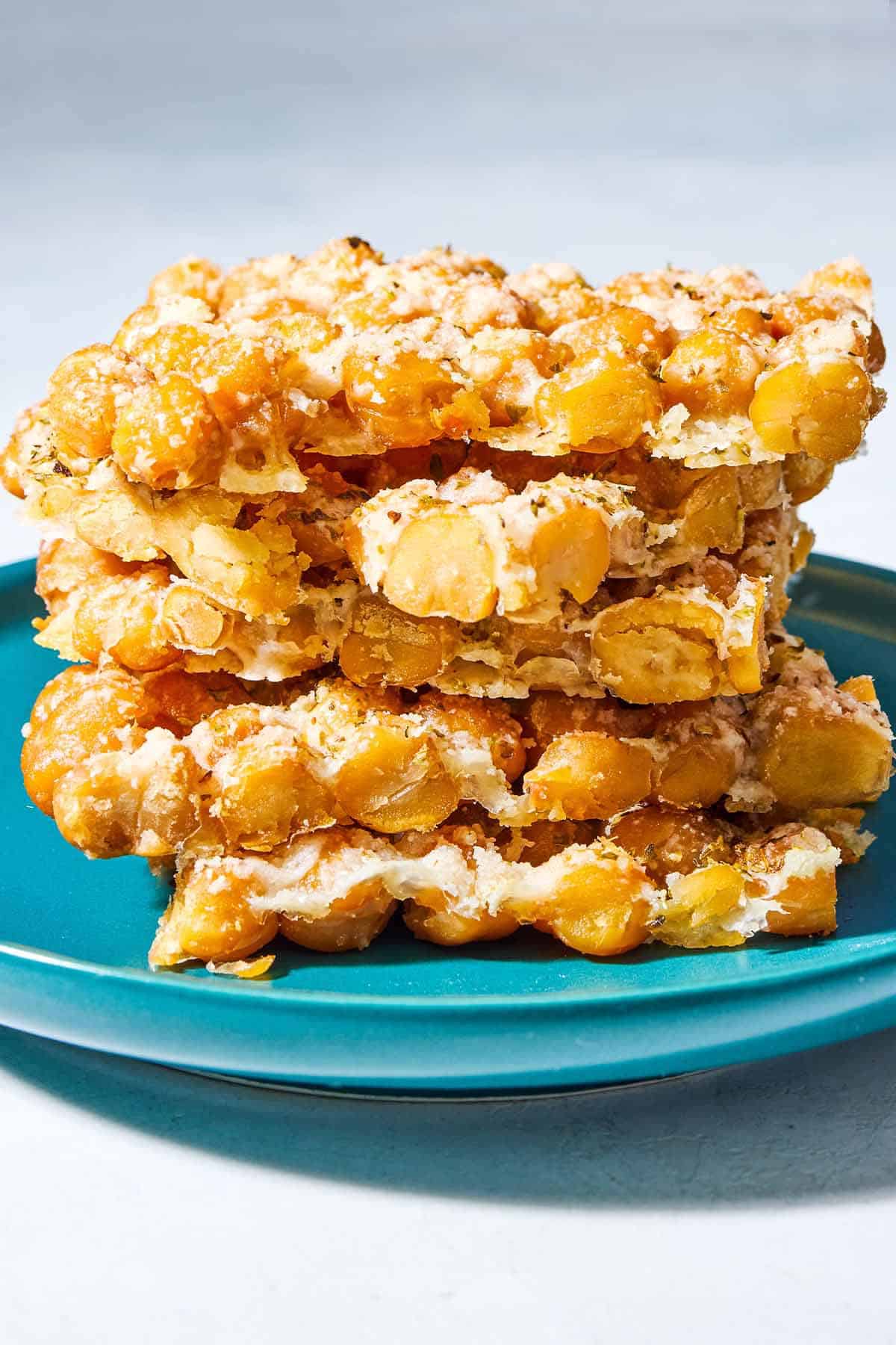 A close up of a stack of 5 baked parmesan crisps with chickpeas and oregano on a plate.