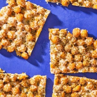 An overhead photo of baked parmesan crisps with chickpeas and oregano cut into 5 slices.