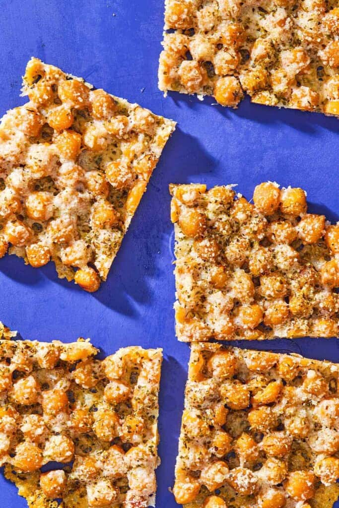 An overhead photo of baked parmesan crisps with chickpeas and oregano cut into 5 slices.