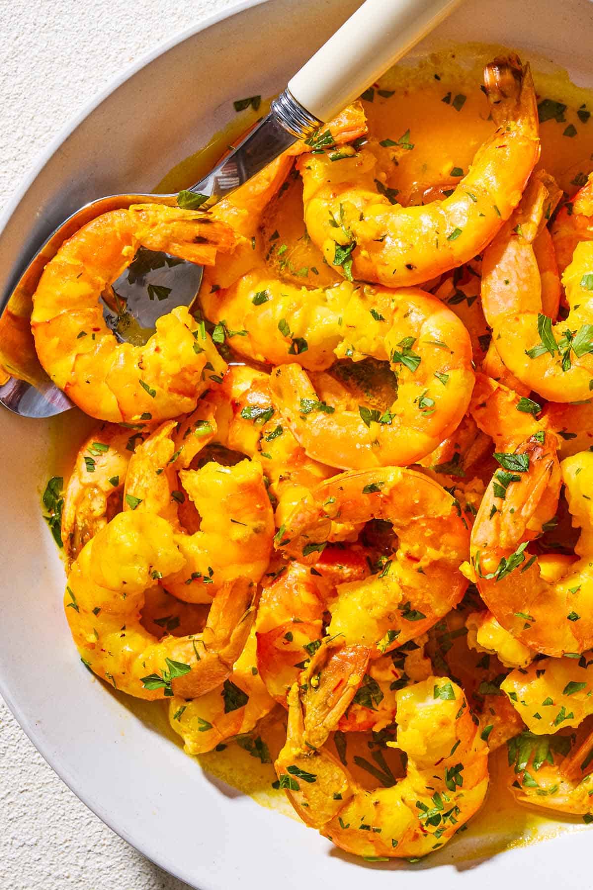 An overhead photo of poached shrimp in a saffron and white wine sauce in a bowl with a spoon.