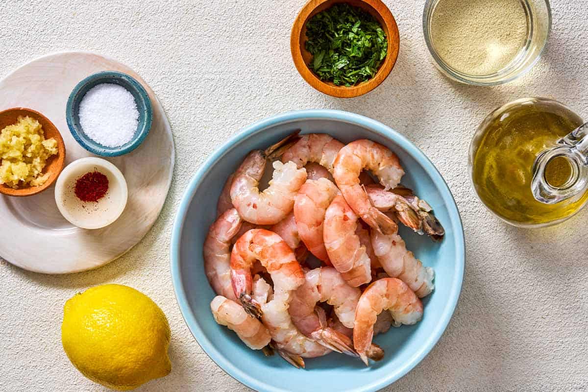 Ingredients for poached shrimp in a saffron and white wine sauce including ground saffron, olive oil, garlic, white wine, lemon, shrimp, salt and chopped parsley.