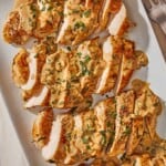 An overhead photo of 4 sliced chicken breasts topped with tarragon mustard sauce on a platter.