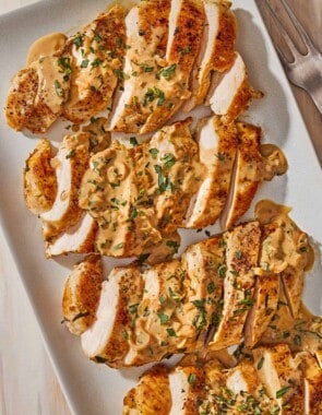 An overhead photo of 4 sliced chicken breasts topped with tarragon mustard sauce on a platter.