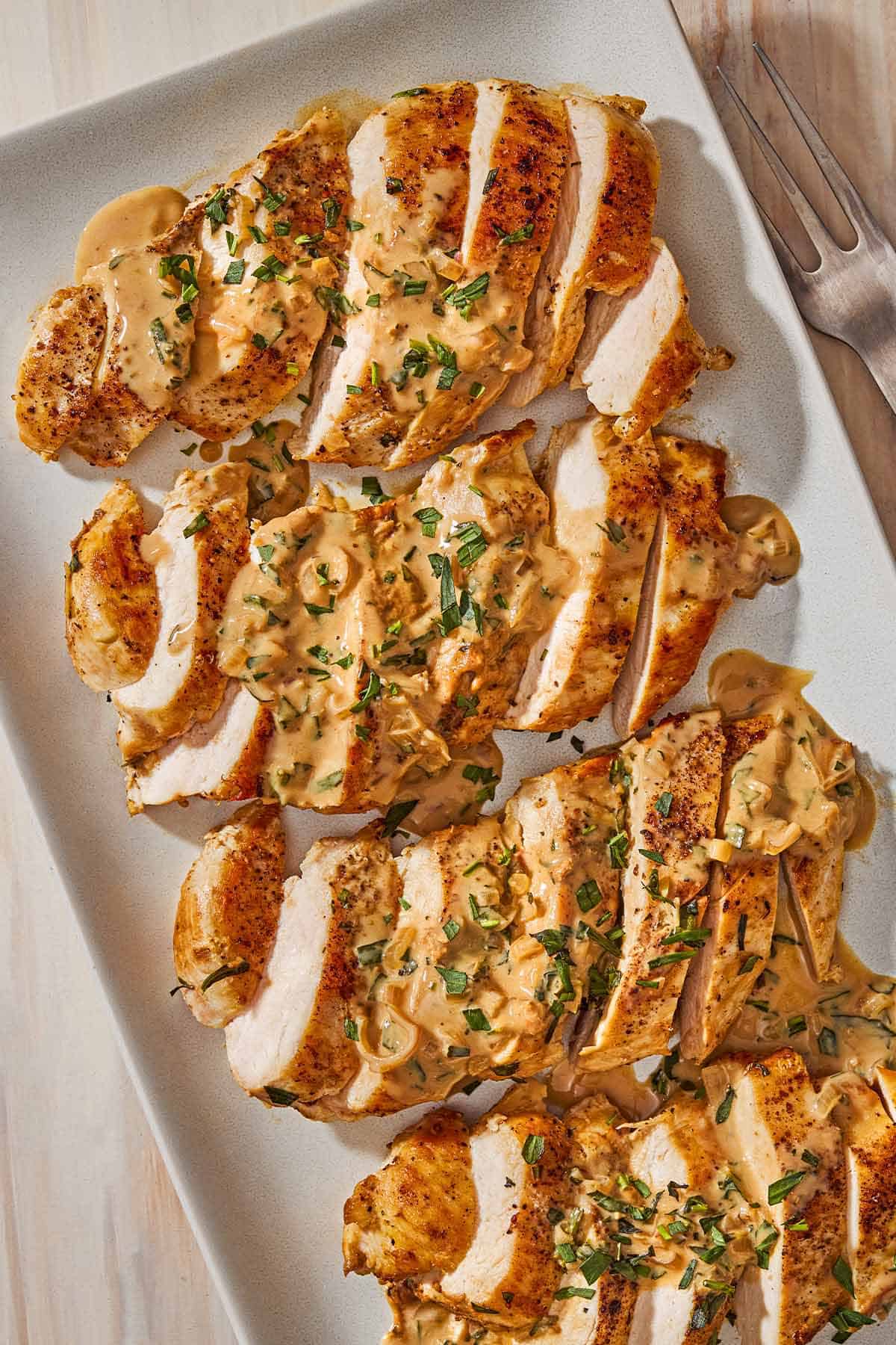 An overhead photo of 4 sliced chicken breasts topped with tarragon mustard sauce on a platter.