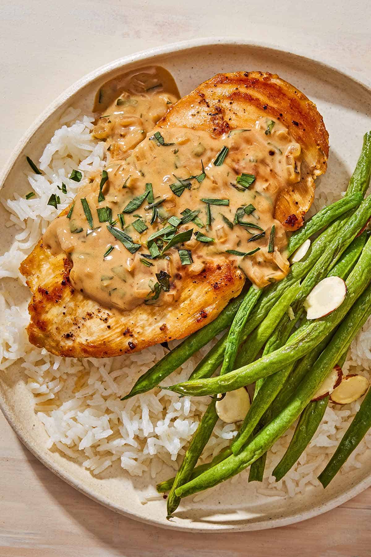 A close up of a serving of chicken with tarragon mustard sauce and green beans on a bed of rice on a plate.