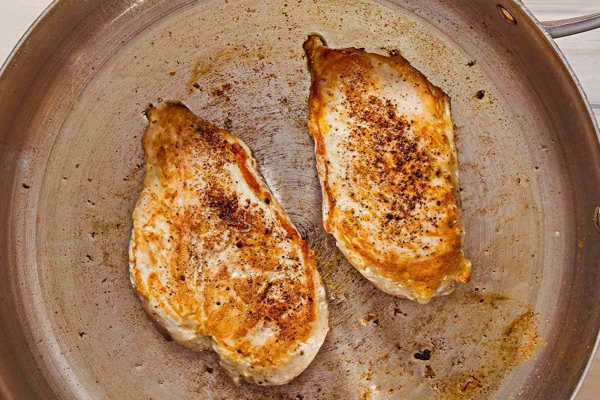 2 chicken breast halves being seared in a skillet.