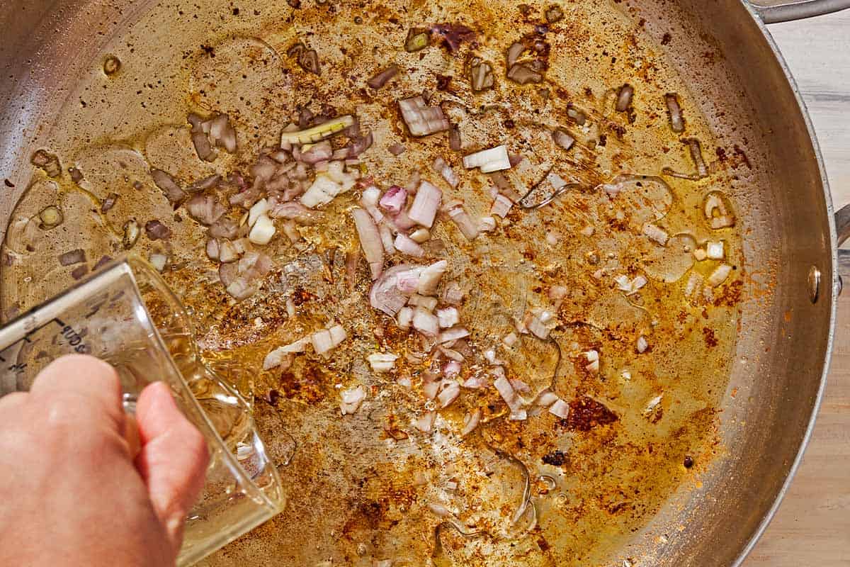 An overhead photo of the wine being added to the skillet with the water and chopped shallots.