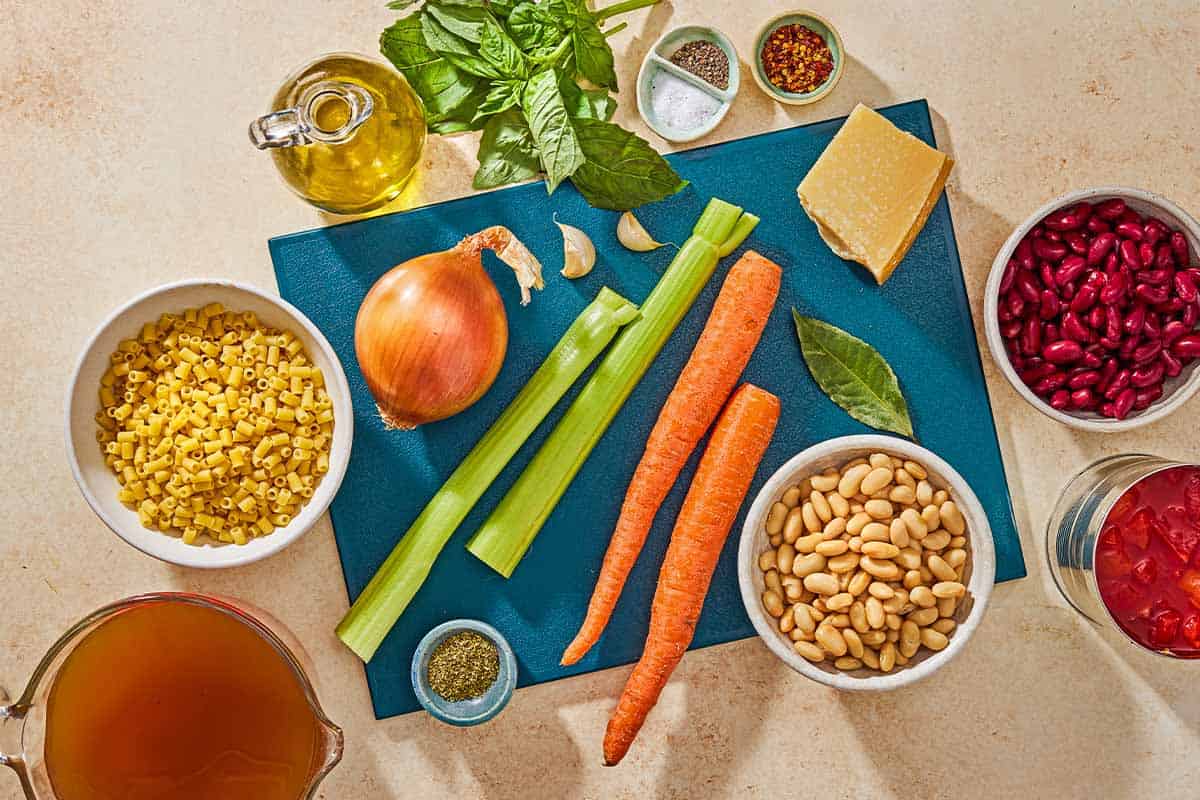 Ingredients for pasta fagioli including pasta, olive oil, onion, celery, carrots, garlic, a bay leaf, dried oregano, fire roasted diced tomatoes, vegetable broth, cannellini beans, kidney beans, salt, black pepper, red pepper flakes, basil and parmesan cheese.