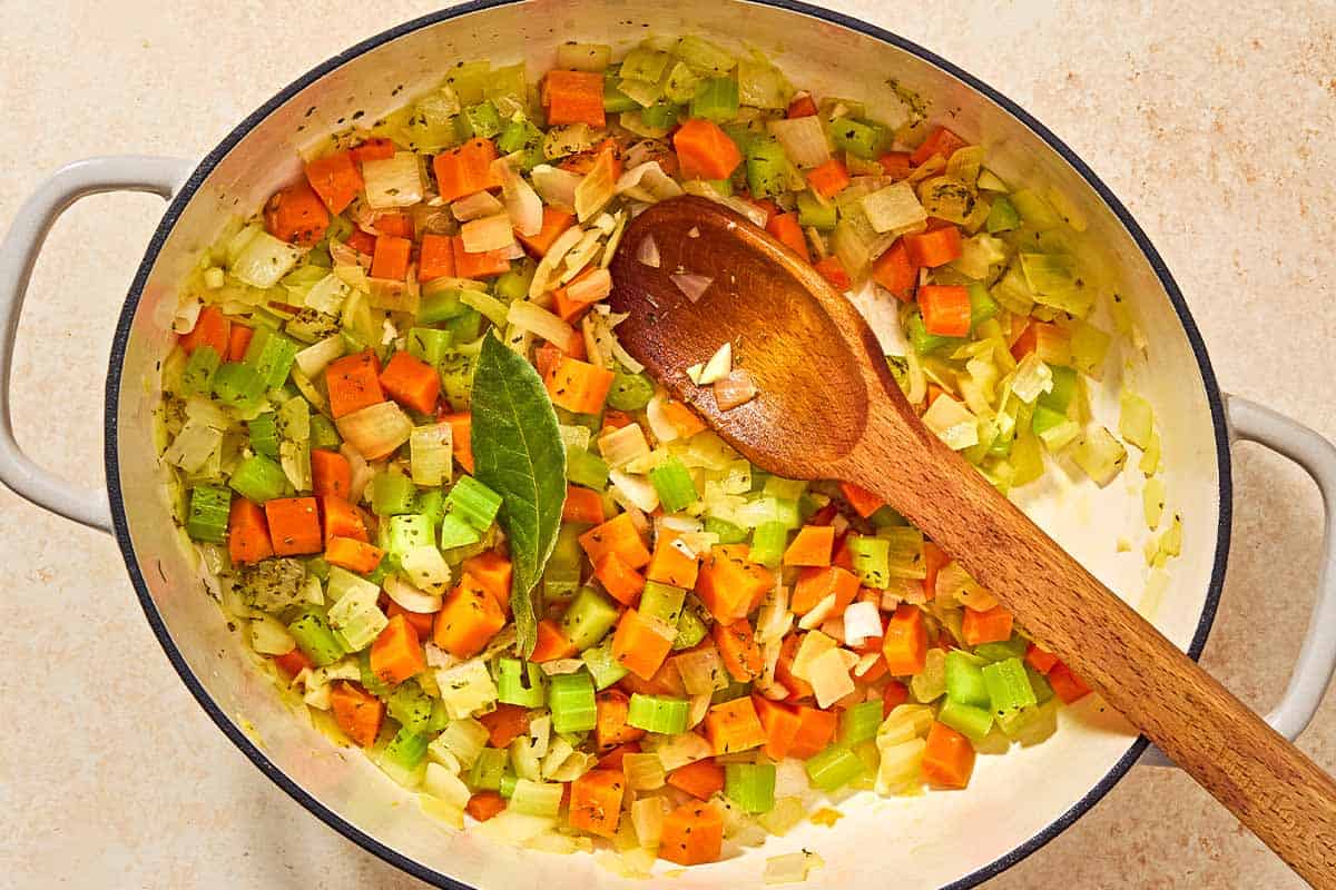 An overhead photo of the chopped vegetables and the bay leaf for the pasta fagioli after being sauteed in a pot with a wooden spoon.