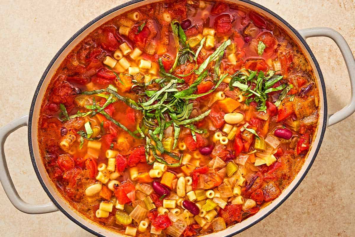 An overhead photo of a pot of pasta fagioli garnished with fresh basil.