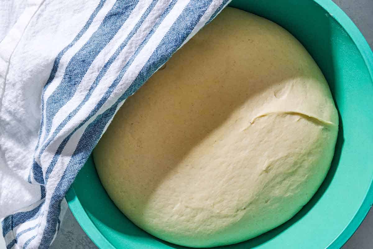 A close up of the dough for the sfincione sicilian pizza in a bowl, partially covered by towel, after resting.